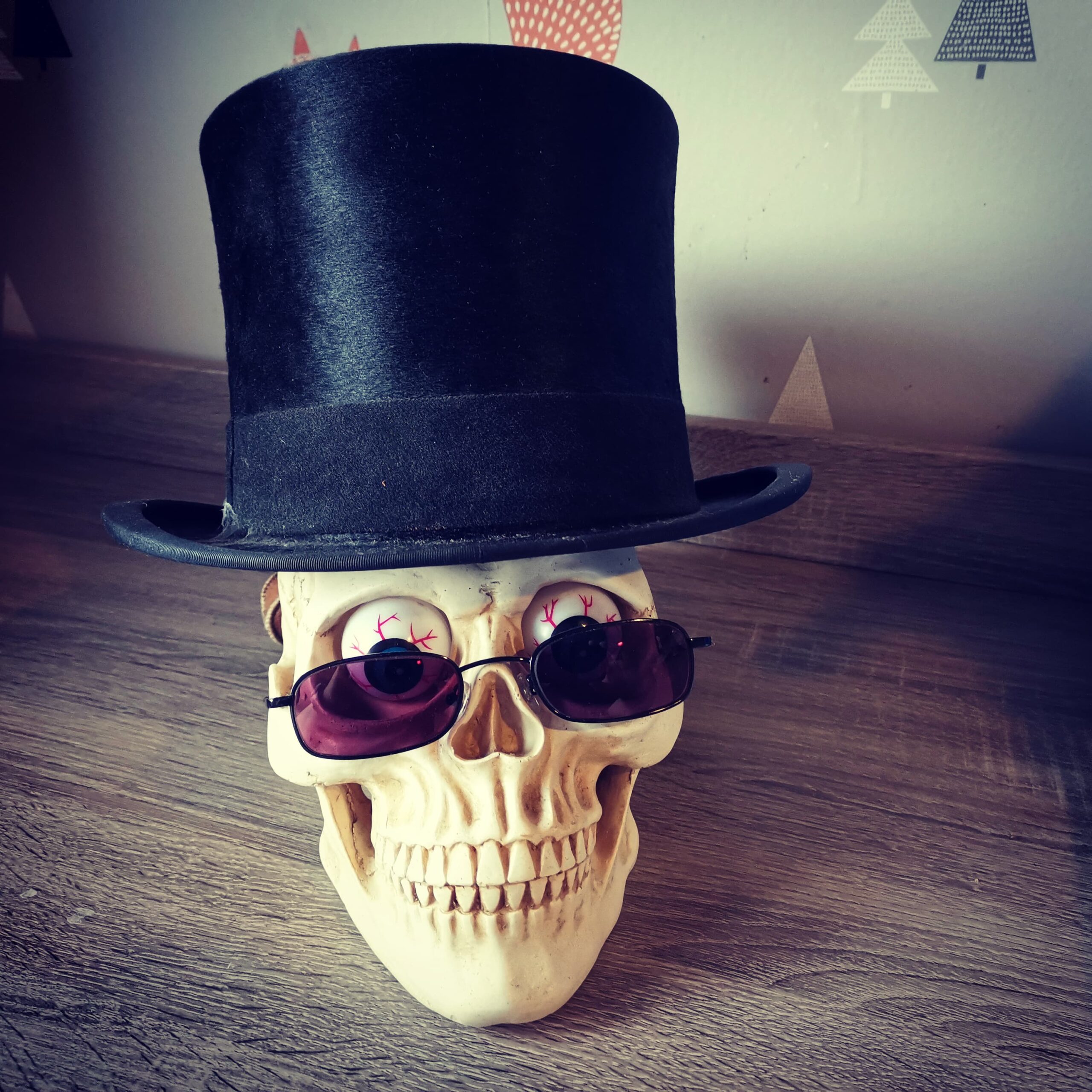 Image of a model human skull with plastic eyeballs (aka Erik), wearing a top hat and a pair of red-tinted sunglasses.