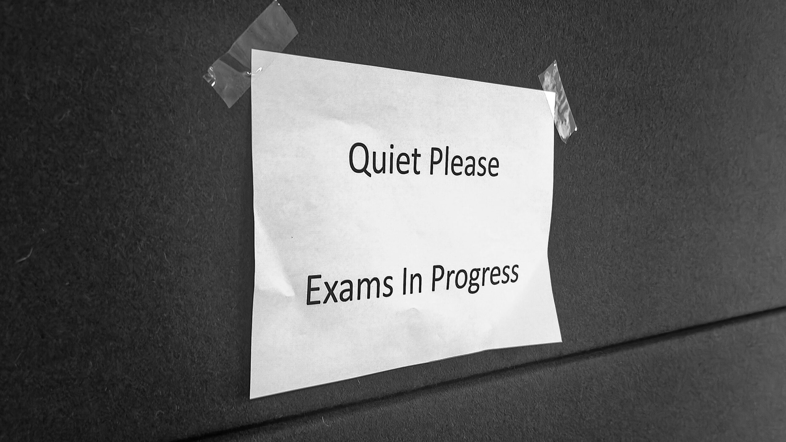 A paper sign on a wall stating "Quiet Please Exams In Progress".